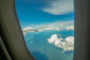 vista de dentro do avião através da janela do avião sobre o céu azul, nuvens brancas e montanha verde. vôo de companhia aérea comercial para viagens de verão. asa de avião acima da cidade. avião voando acima da terra. foto