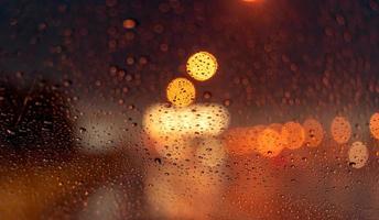bokeh de luz noturna laranja da luz da rua no dia do engarrafamento. dia chuvoso. janela de vidro transparente com gota de chuva. clima romântico. vida urbana. desfocar o fundo abstrato da luz urbana na estação chuvosa foto