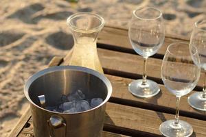 garrafa de vinho, copos e gelo na mesa de madeira, fundo de praia de verão foto