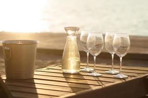 garrafa de vinho, copos e gelo na mesa de madeira, fundo de praia de verão foto