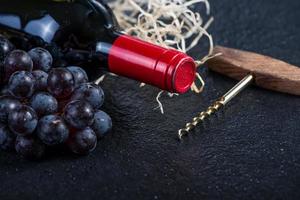 garrafa de vinho vermelha com uvas e saca-rolhas