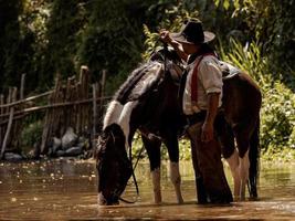 velho cowboy descansou com um cavalo no riacho depois que ele terminou de dar banho no cavalo foto