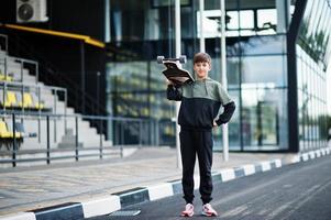 menino adolescente em um terno esportivo com longboard. foto