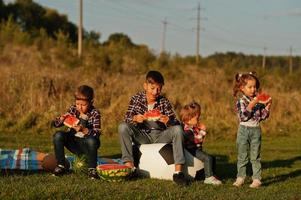 família passar tempo juntos. quatro crianças comem melancia ao ar livre. foto