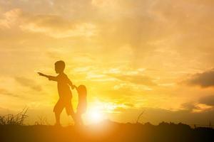 silhueta de menino e menina brincando no fundo por do sol, conceito de crianças felizes. foto