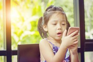 menina bonitinha olhando para cima pensando e segurando smartphone, conceito de criança feliz foto