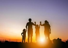 silhueta de pai mãe e dois filhos se divertindo no pôr do sol, conceito de família feliz. foto