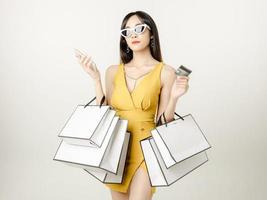 mulher asiática confiante em um vestido amarelo sensual usando óculos escuros e carregando uma sacola de compras está se divertindo fazendo compras. foto