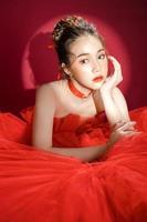 modelo de jovem mulher bonita asiática em um elegante vestido vermelho de luxo elegante sobre um fundo vermelho isolado.