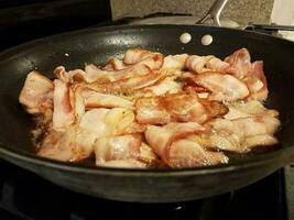 bacon cozinhando na frigideira ou frigideira no fogão foto