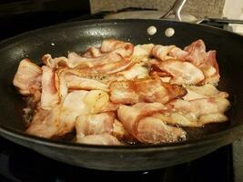 bacon cozinhando na frigideira ou frigideira no fogão foto