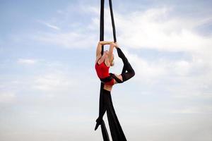 exercícios com seda aérea ao ar livre, fundo do céu. bela mulher em forma de treinamento acrobático no ar. foto