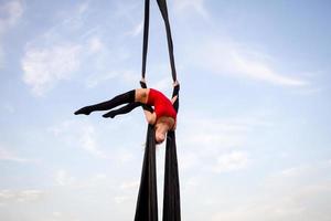 exercícios com seda aérea ao ar livre, fundo do céu. bela mulher em forma de treinamento acrobático no ar. foto