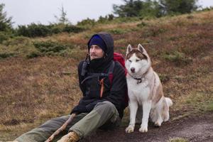 jovem macho com cachorro husky nas montanhas, viajar com cães foto