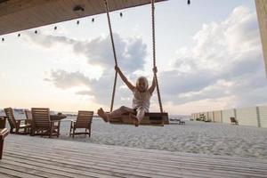 menina loira desfrutar de balanço na praia, férias de verão foto