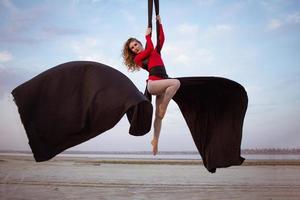 exercícios com seda aérea ao ar livre, fundo do céu. bela mulher em forma de treinamento acrobático no ar. foto