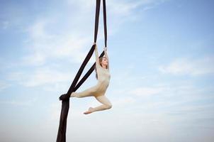 exercícios com seda aérea ao ar livre, fundo do céu. bela mulher em forma de treinamento acrobático no ar. foto