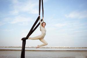 exercícios com seda aérea ao ar livre, fundo do céu. bela mulher em forma de treinamento acrobático no ar. foto