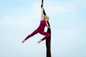 exercícios com seda aérea ao ar livre, fundo do céu. bela mulher em forma de treinamento acrobático no ar. foto