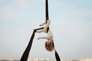 exercícios com seda aérea ao ar livre, fundo do céu. bela mulher em forma de treinamento acrobático no ar. foto