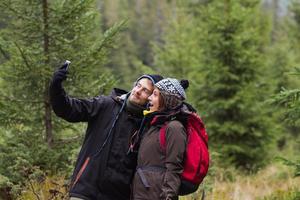 jovem casal caminhante com copos térmicos na floresta, viajantes em montanhas bebendo chá ou café foto