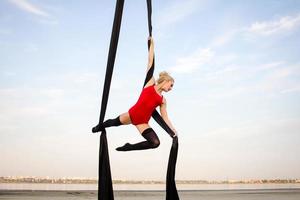 exercícios com seda aérea ao ar livre, fundo do céu. bela mulher em forma de treinamento acrobático no ar. foto