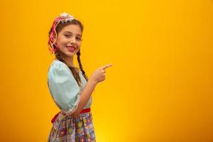 criança em roupas típicas da famosa festa brasileira chamada festa junina em comemoração a são joao. linda garota em fundo amarelo. foto