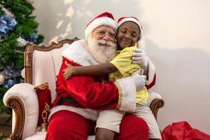 papai noel entregando uma caixa de presente para um menino africano. abraço. véspera de natal, entrega de presentes. foto