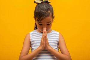 menina rezando sobre fundo amarelo. mão de menina asiática rezando, mãos dobradas no conceito de oração para fé, espiritualidade e religião. foto