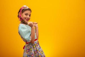 criança em roupas típicas da famosa festa brasileira chamada festa junina em comemoração a são joao. linda garota em fundo amarelo. foto