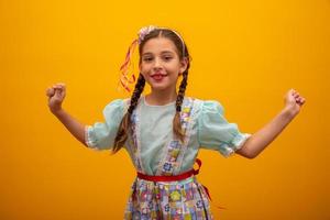 criança em roupas típicas da famosa festa brasileira chamada festa junina em comemoração a são joao. linda garota em fundo amarelo. foto