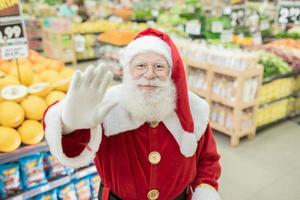 papai noel fazendo compras no supermercado, ele está empurrando um carrinho cheio, natal e conceito de compras. foto