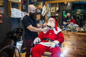 Papai Noel se barbeando na barbearia. olhando no espelho. se preparando para o natal. embelezamento para as férias. barbudo. corte. foto