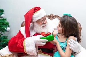 papai noel entregando uma caixa de presente para uma garotinha. véspera de natal, entrega de presentes. foto