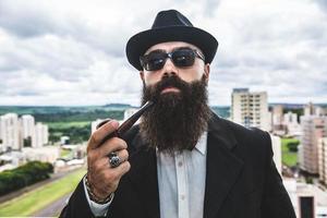 elegante homem barbudo fumando cachimbo olhando para o horizonte do topo de um prédio alto. foto