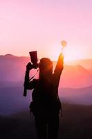 mulher jovem viajante levante as mãos para seu sucesso com o pôr do sol no fundo natural da montanha. foto