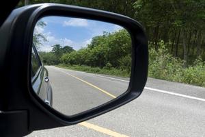 visão interna da asa dos espelhos. vista traseira de um carro cinza com estrada de asfalto e árvores verdes durante o dia. trânsito livre nas áreas rurais. foto