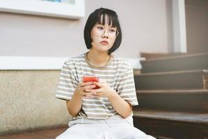 jovem mulher asiática adulta usa óculos usando telefone celular. foto