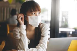 jovem mulher asiática adulta com máscara facial protetora para vírus covid 19 trabalha e estuda no café no dia.
