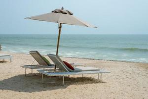 duas espreguiçadeiras e guarda-chuva na praia tropical - tempo de férias foto