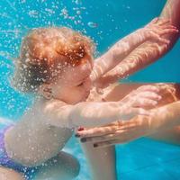 sorridente menina mergulho azul piscina subaquática. estilo de vida ativo, aula de natação infantil com os pais. atividade de esportes aquáticos durante as férias de verão em família no resort tropical foto