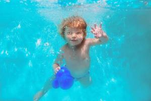 bonito sorrindo adorável menina mergulho piscina azul subaquática. estilo de vida ativo, aula de natação infantil. atividade de esportes aquáticos durante as férias de verão em família no resort tropical foto