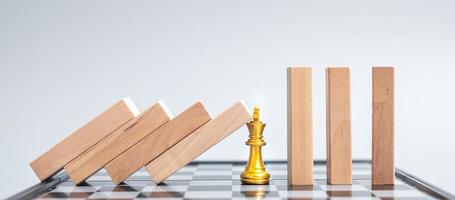 blocos de madeira ou dominó caindo para a figura do rei do xadrez dourado. negócios, gestão de risco, solução, regressão econômica, seguro foto