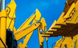 retroescavadeira amarela com braço de pistão hidráulico contra céu azul claro. máquina pesada para escavação no canteiro de obras. máquinas hidráulicas. enorme escavadora. industria pesada foto