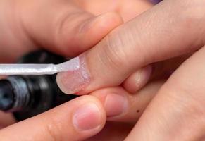 mulher recebendo serviço de manicure de unha por manicure profissional no salão de beleza. esteticista pintando unhas no salão de unhas e spa. focado em esmalte branco e glitter no salão de beleza. foto