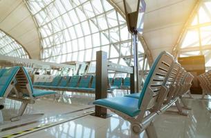 foco seletivo no assento na sala de embarque no terminal do aeroporto. distância para um assento mantenha distância para proteger o distanciamento social do coronavírus e dos passageiros. janela de vidro no terminal do portão do aeroporto. foto