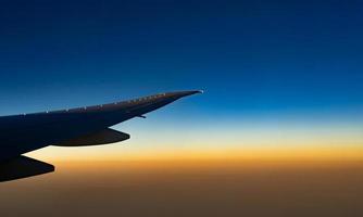 asa de avião sobre a cidade. avião voando no céu azul. vista panorâmica da janela do avião. voo comercial da companhia aérea pela manhã com luz solar. asa de avião acima das nuvens. conceito de mecânica de voo. foto