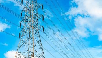 torre elétrica de alta tensão e linhas de transmissão. postes de eletricidade com céu azul e nuvens brancas. potência e conservação de energia. torre de grade de alta tensão com cabo de arame na estação de distribuição. foto