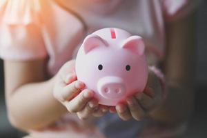 criança mulher mão segura cofrinho rosa para economizar dinheiro para estudo ou investimento em educação, economizar dinheiro conceito, mãos de filha segurando cofrinho rosa foto