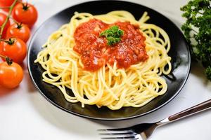 macarrão italiano espaguete servido na chapa preta com tomate e salsa no restaurante comida italiana e conceito de menu - vista superior de espaguete à bolonhesa foto